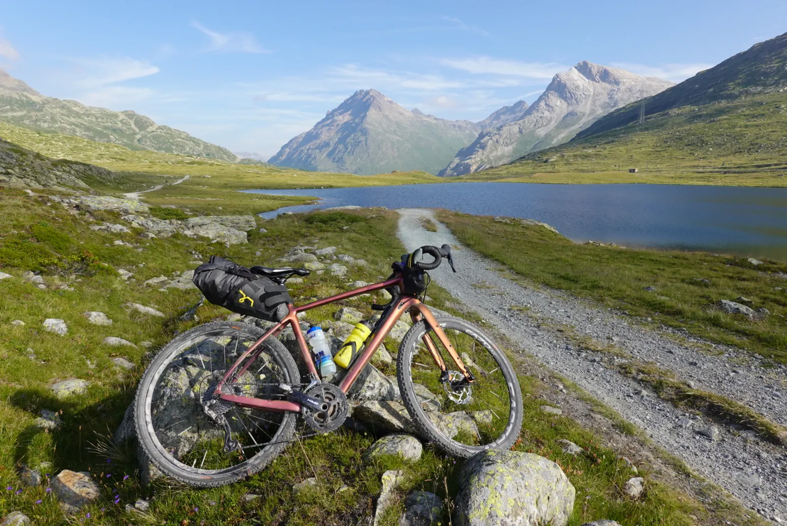 Das bepackte Gravelbike an einem Gravelweg am Bergsee, dahinter hohe Gipfel