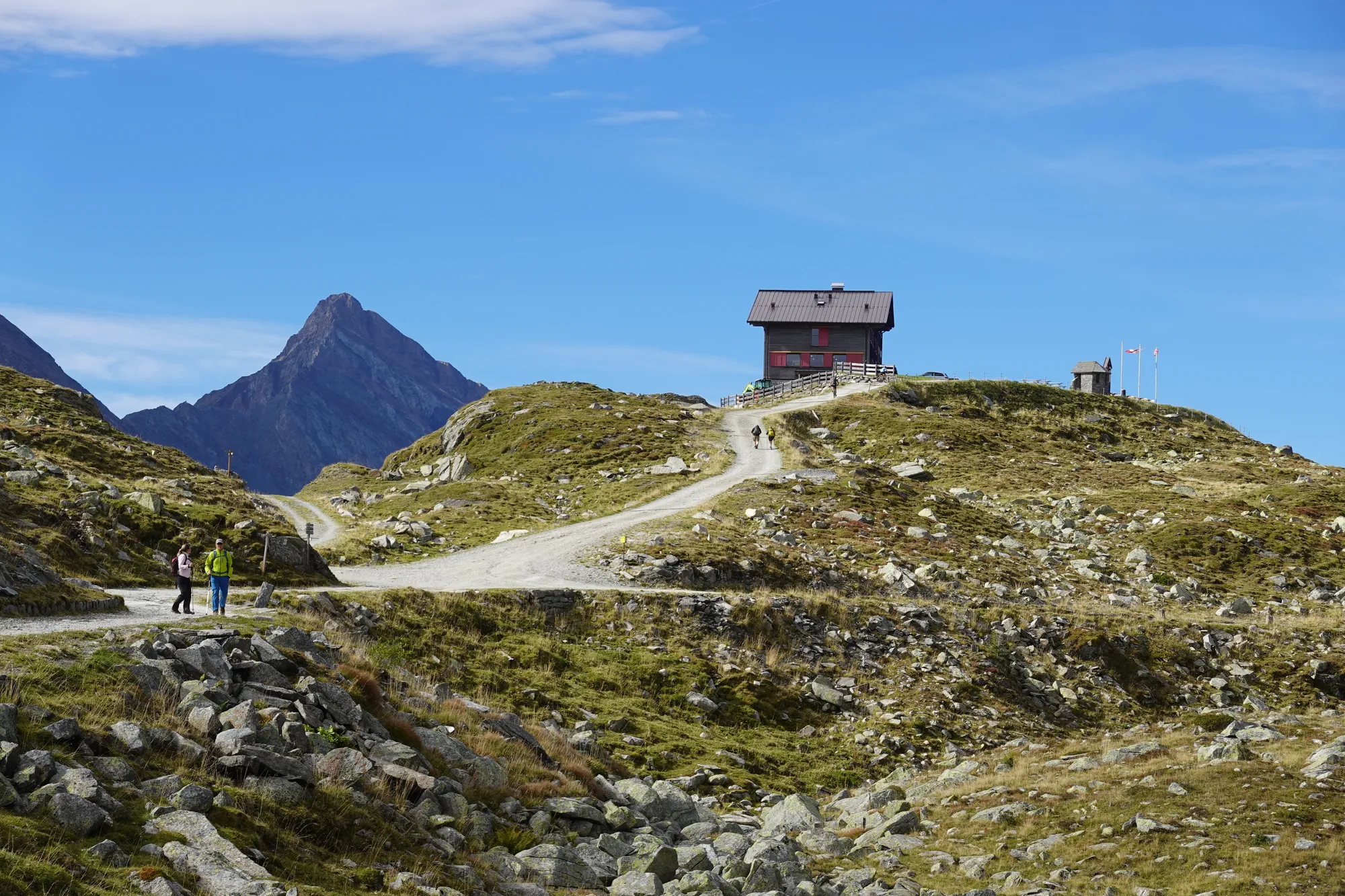 Das Pfitscherjochhaus auf der Passhöhe, davor ein Gravelweg mit Wanderern