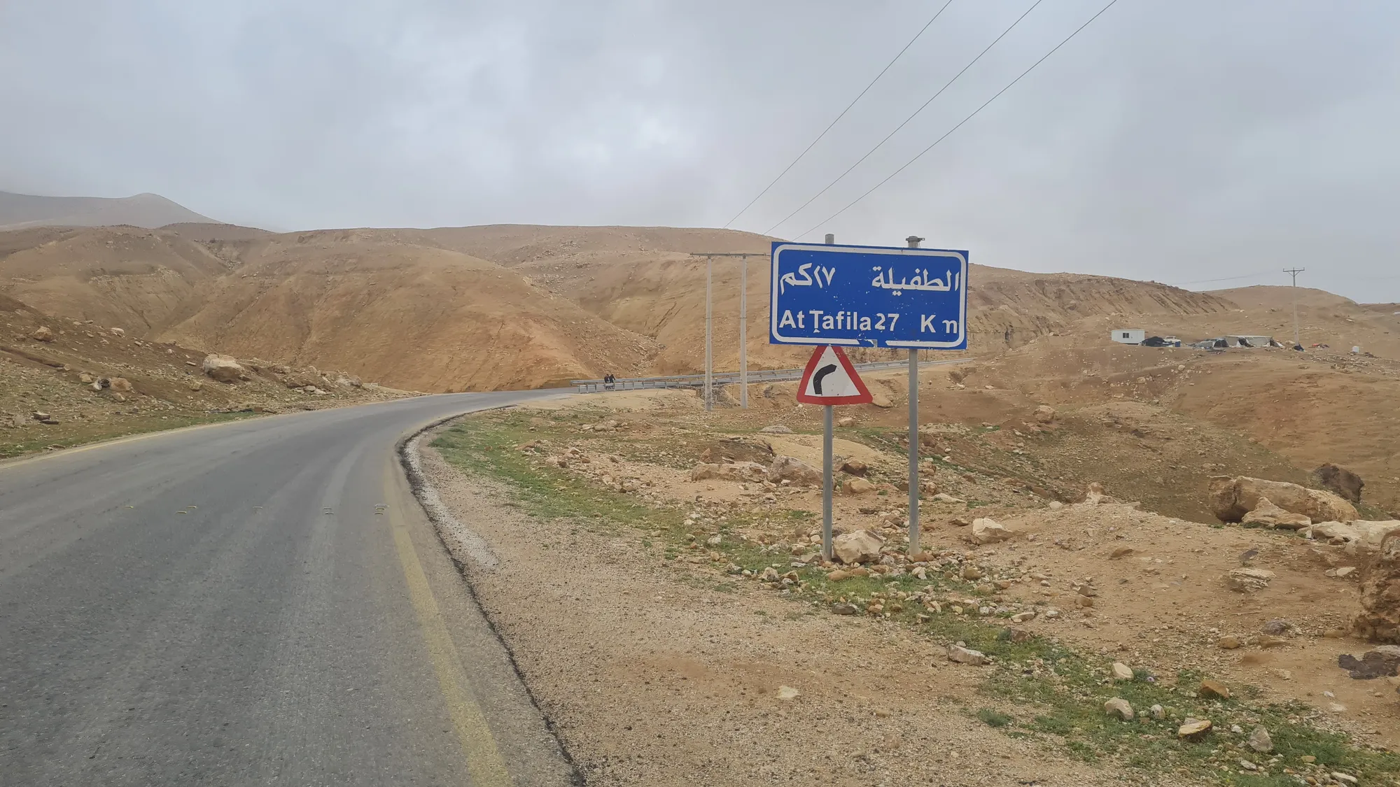 Straßenschild nach Tafila, dahinter Wolken über den Bergen