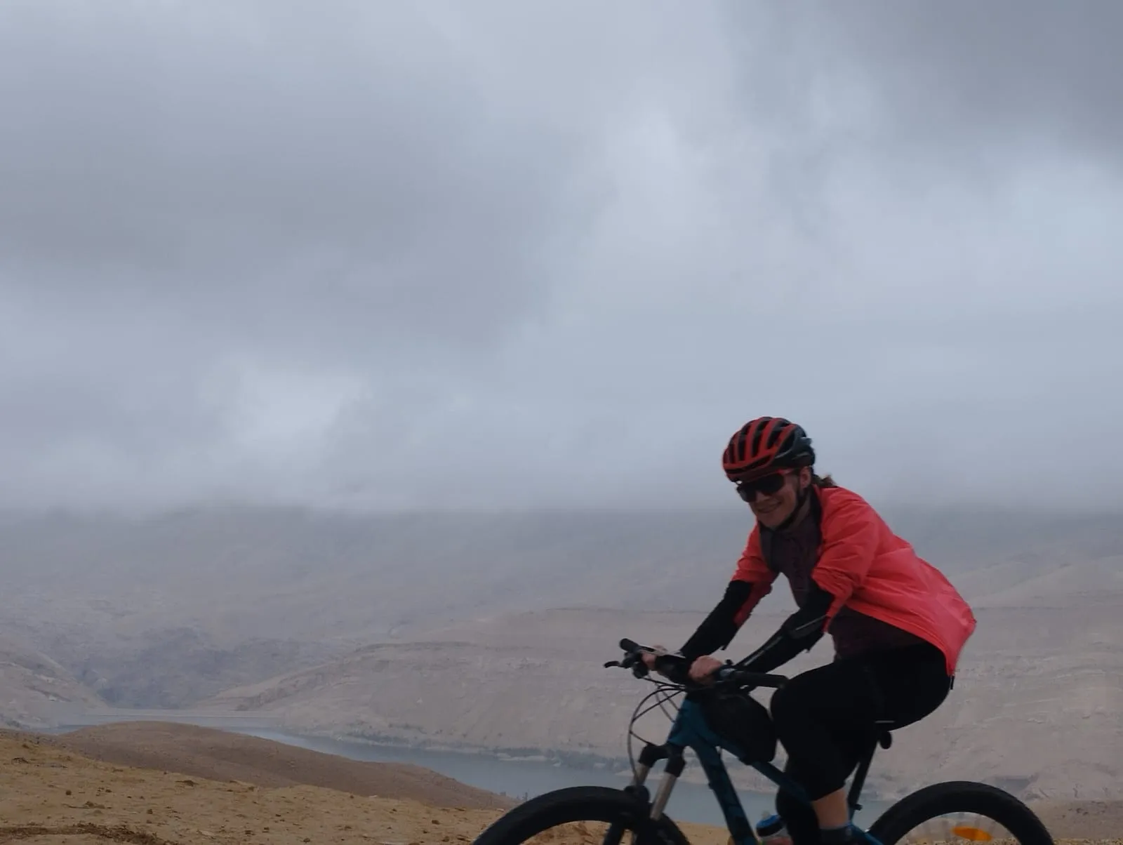 Auf dem Mountainbike unter tief hängenden Wolken, dahinter das Tal