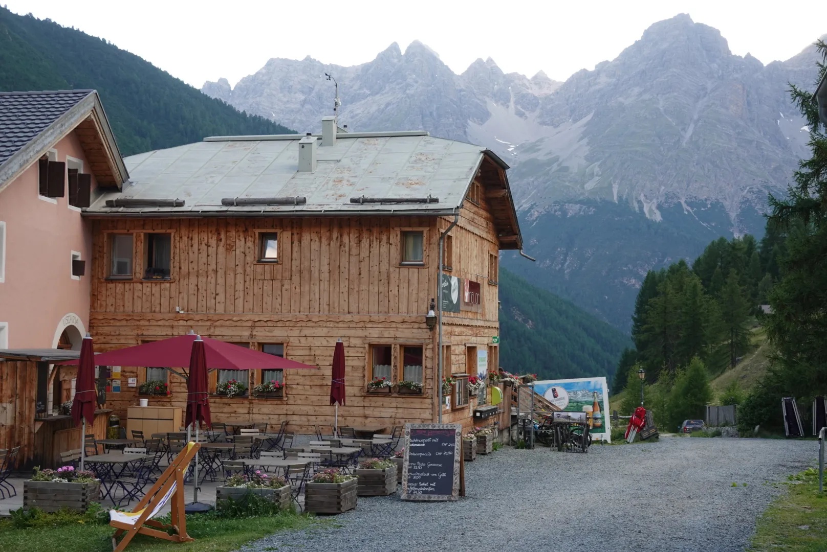 Das Gasthaus in S-charl mit Holzfassade und Sonnenschirmen vor felsigen Bergen