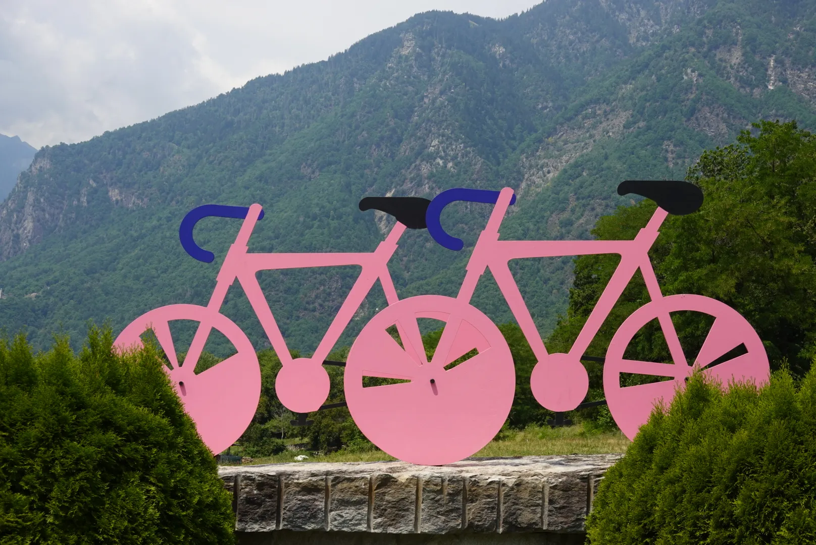 Zwei rosa Fahrradfiguren vor grünen Bergen