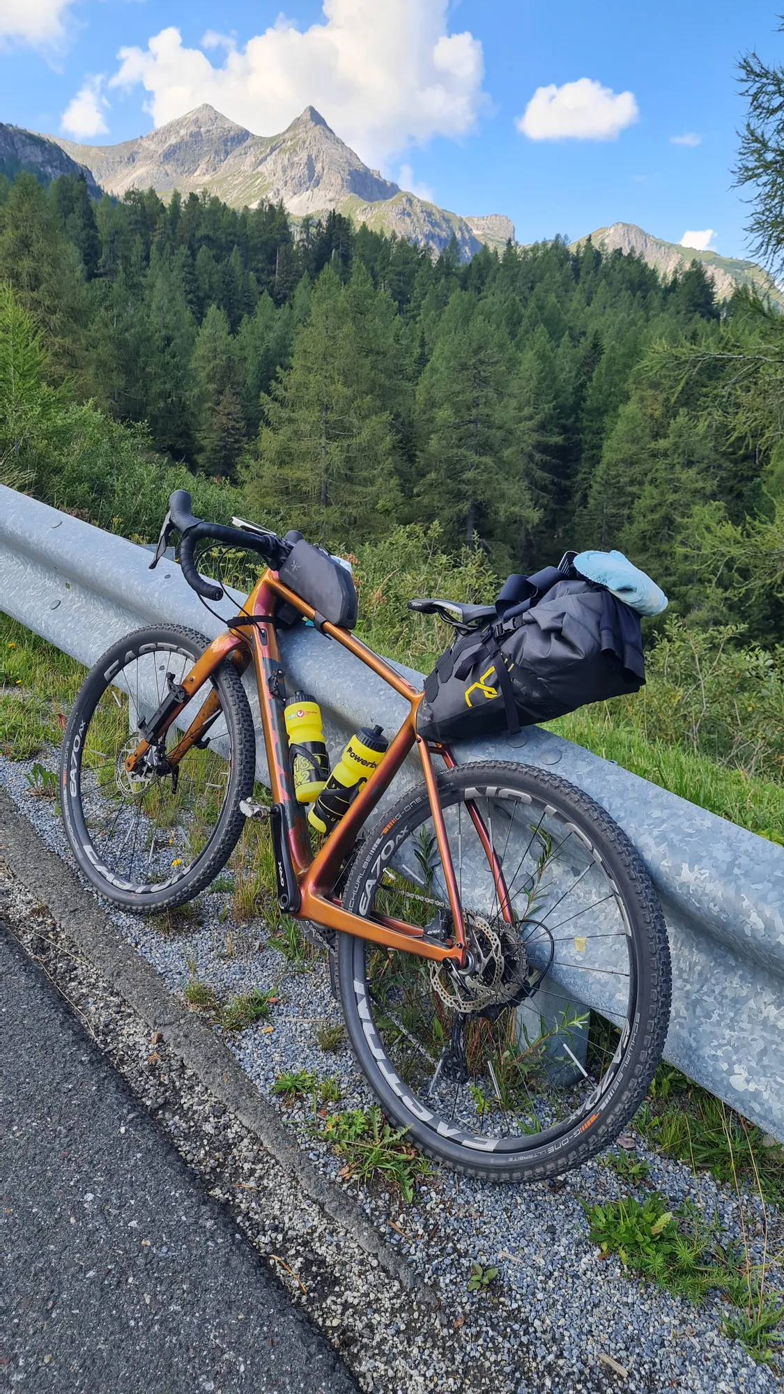 Bepacktes Gravelbike an der Leitplanke, dahinter ein spitzer Gipfel