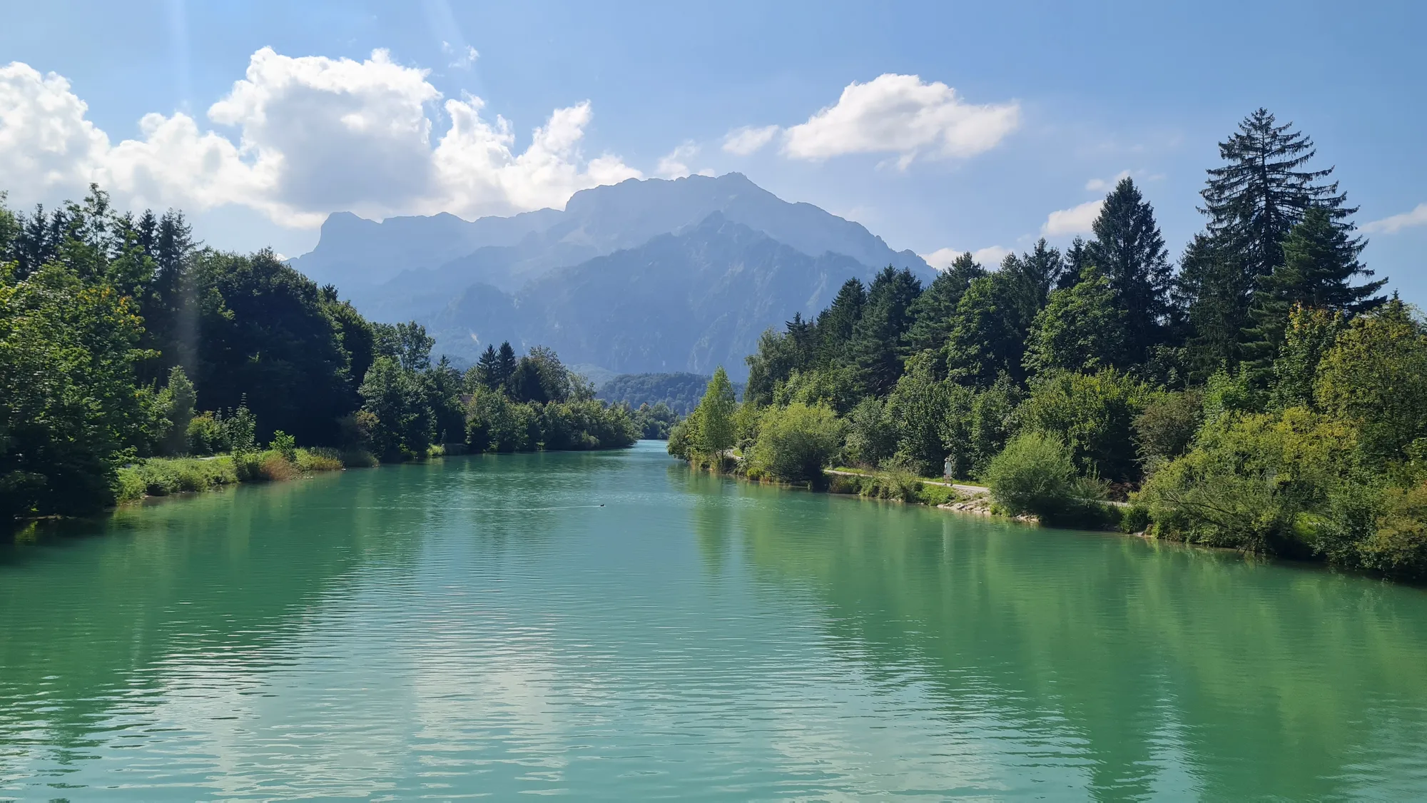 Türkisfarbener Fluss zwischen Wald, dahinter ein Bergmassiv