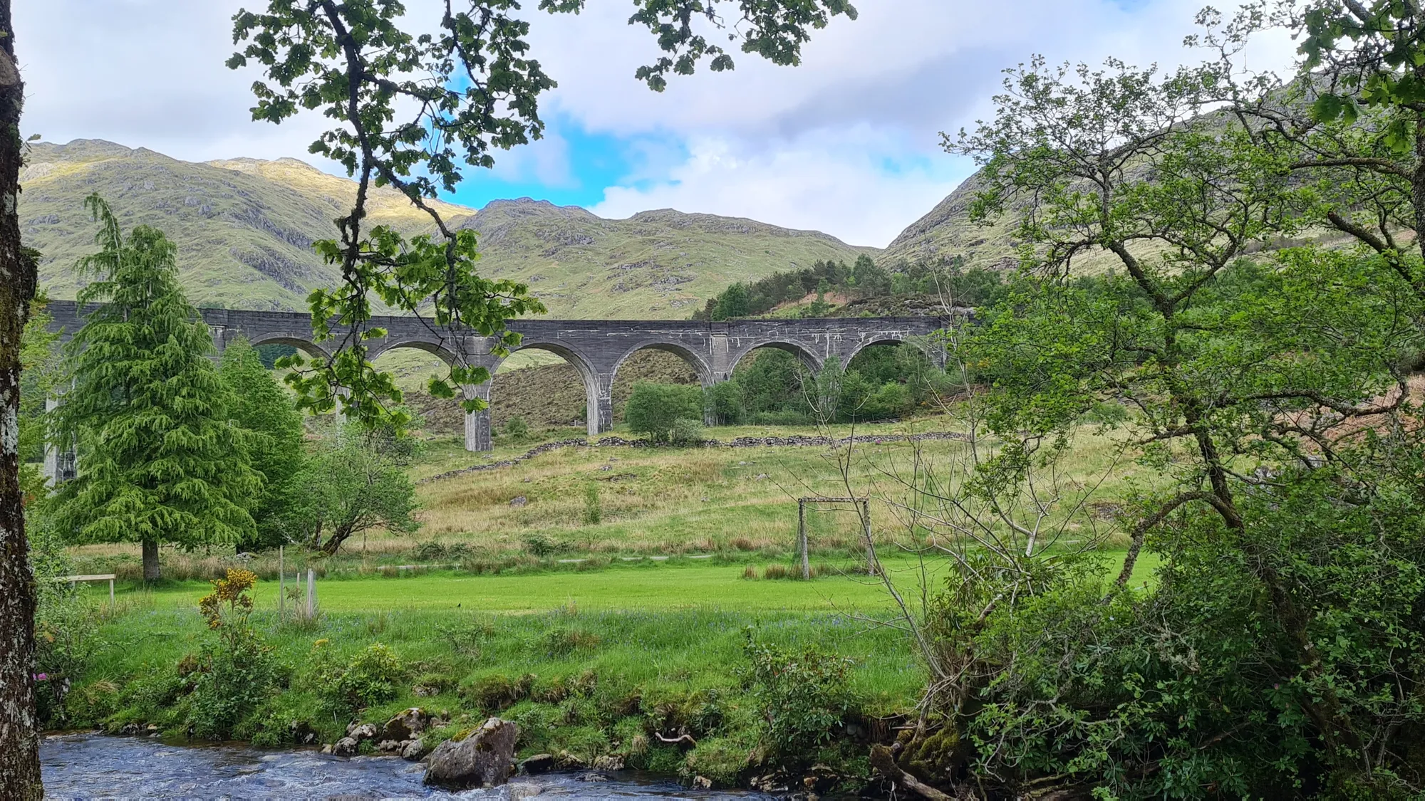 Das Glenfinnan-Viadukt hinter Bäumen und einem Bach