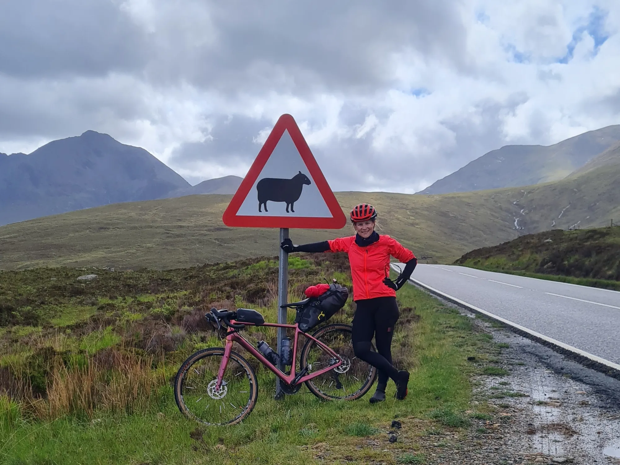 Carla mit dem Rad am Schafe-Warnschild, dahinter dunkle Berge