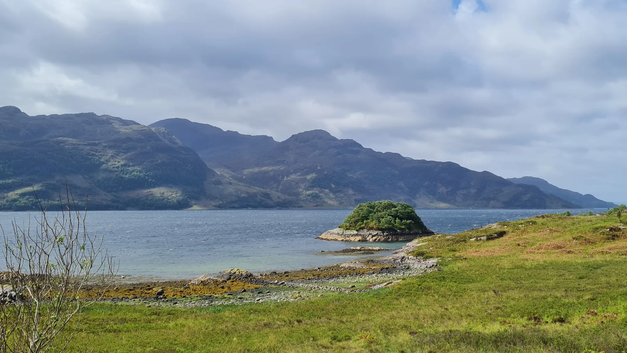 Küste mit kleiner Insel und Bergen auf der anderen Seite des Lochs