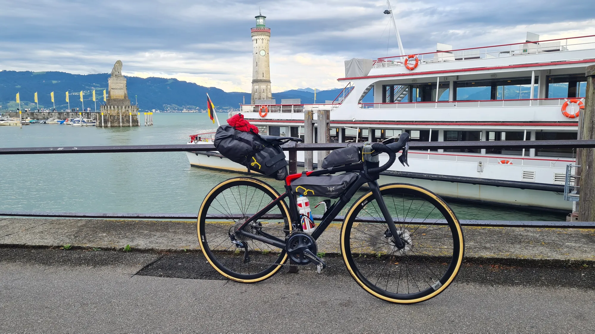Bepacktes Rennrad am Hafen von Lindau, dahinter Leuchtturm und Ausflugsschiff
