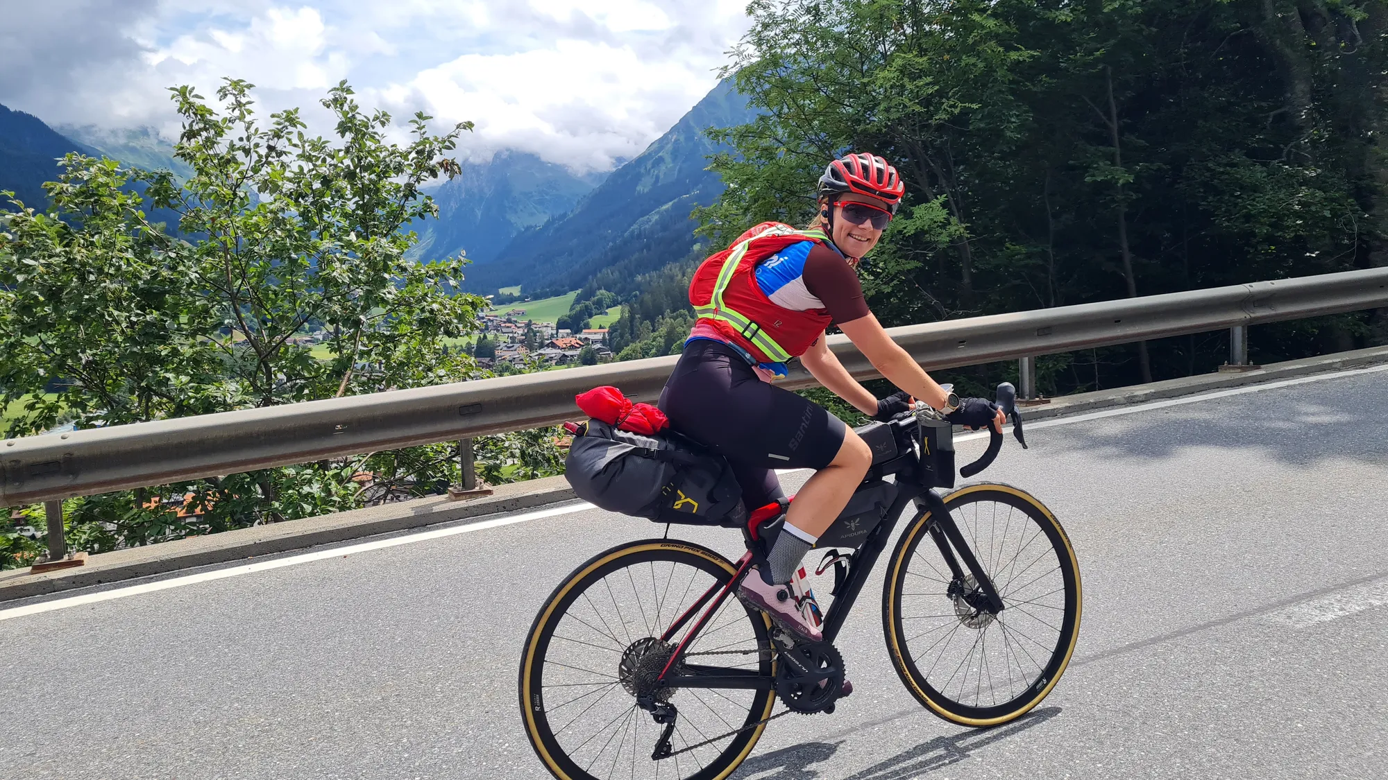 Ich auf dem bepackten Rennrad, hinter mir ein grünes Tal mit Wolken
